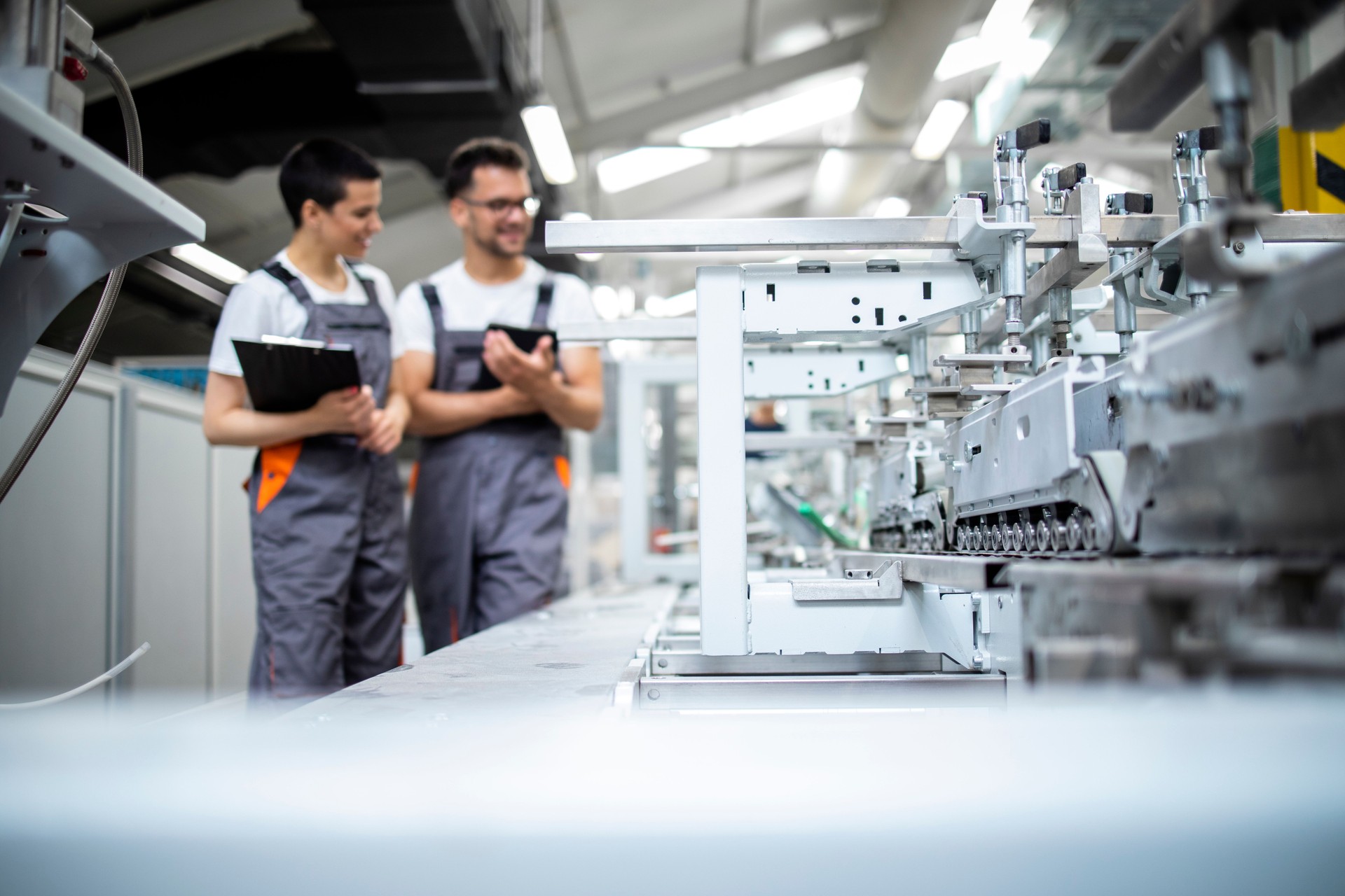 Production line workers controlling manufacturing process of modern packaging industrial machine in factory.